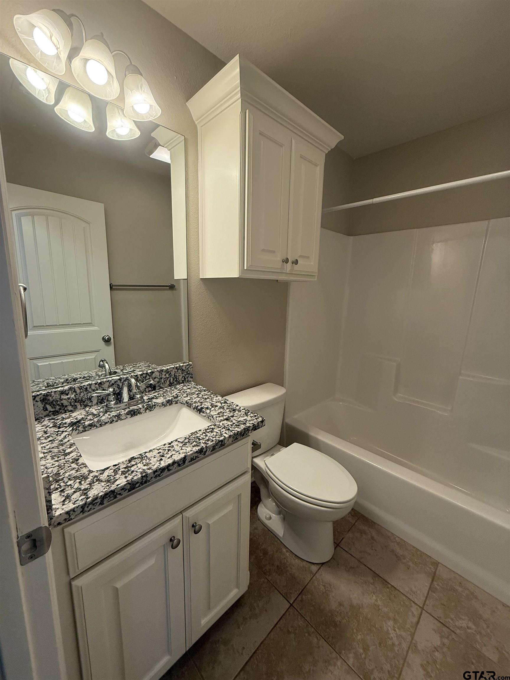 16440 County Road 178, Unit 1007 Tyler, TX 75703 - Photo 20 of 25 a bathroom with a granite countertop sink a toilet a mirror and bathtub