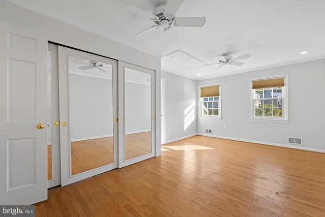 an empty room with wooden floor ceiling fan and windows