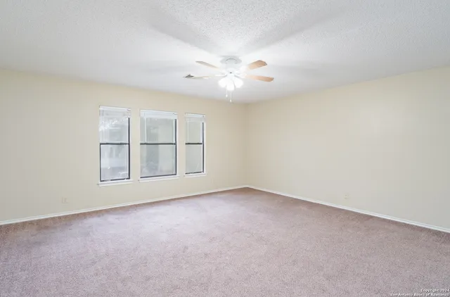 an empty room with chandelier fan and windows