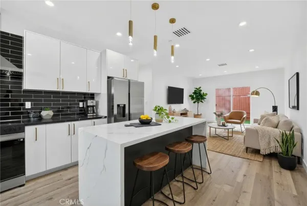 a kitchen with stainless steel appliances kitchen island granite countertop a stove a sink a refrigerator and white cabinets with wooden floor