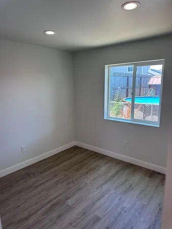 a view of an empty room with wooden floor and a window