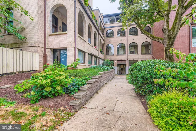 a view of a brick house with a yard plants and large tree