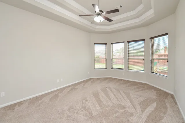 an empty room with chandelier fan and windows