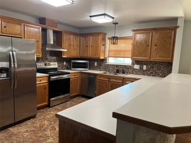 a kitchen with stainless steel appliances a sink a stove a refrigerator cabinets and a window