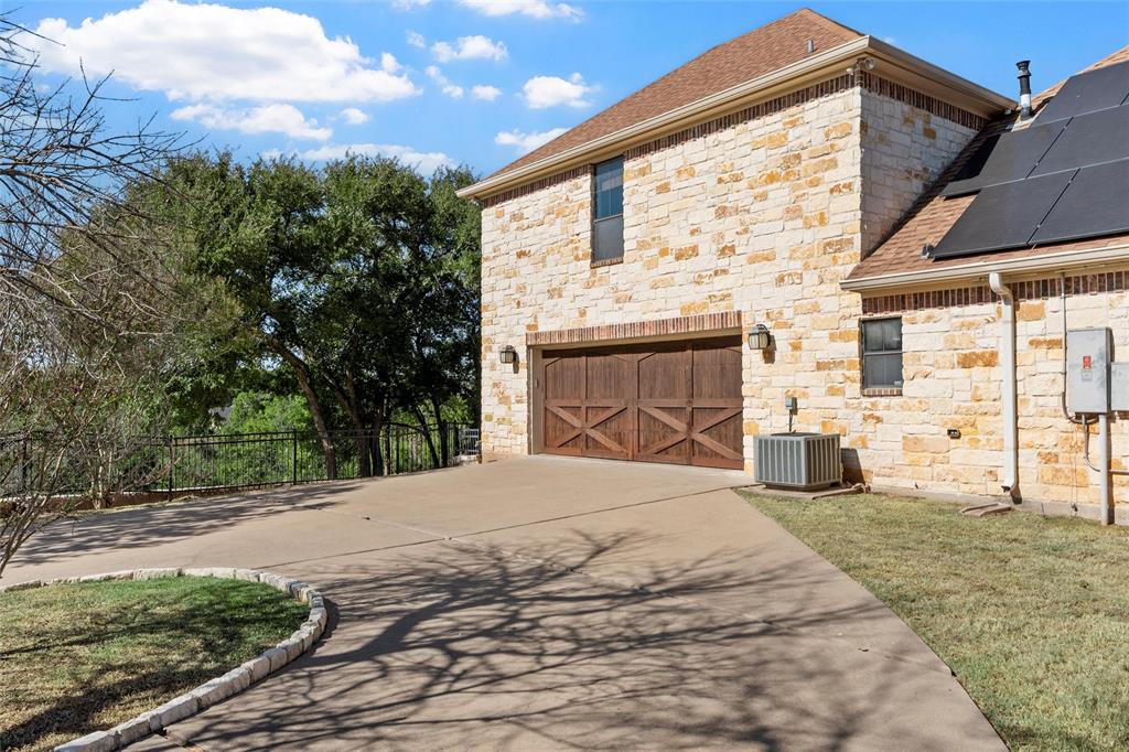 1125 Whispering Oaks China Spring, TX 76633 - Photo 37 of 39 View of side of home featuring roof mounted solar panels, concrete driveway, stone siding, and a shingled roof