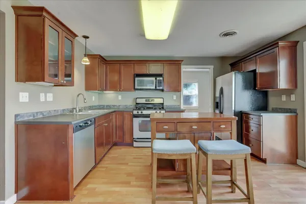 a kitchen with stainless steel appliances granite countertop a stove top oven a sink a refrigerator white cabinets and wooden floor