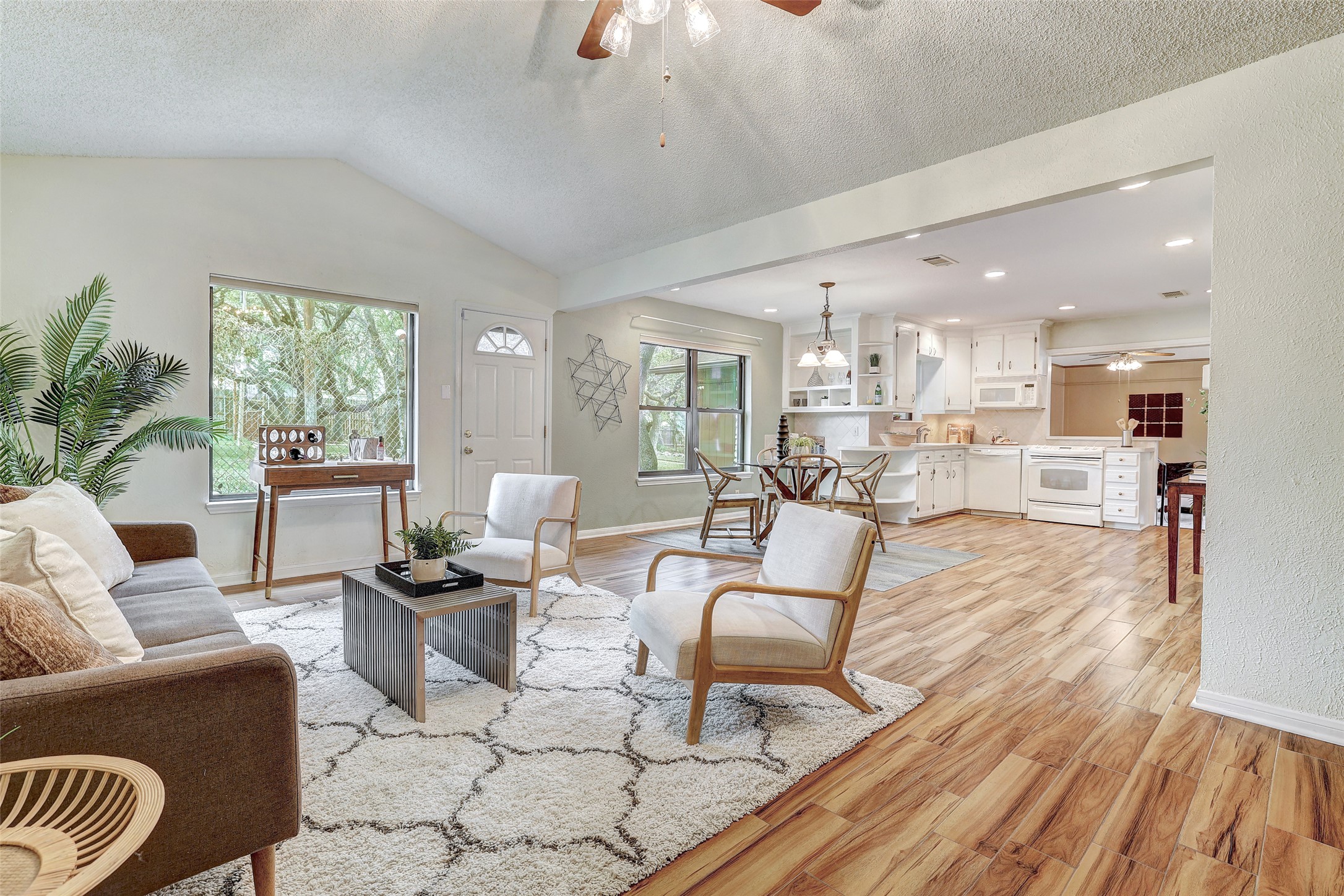 Living room featuring ceiling fan, a textured ceiling, light wood-type flooring, and vaulted ceiling, windows facing huge private backyard