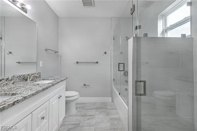 a bathroom with a granite countertop shower sink vanity and toilet