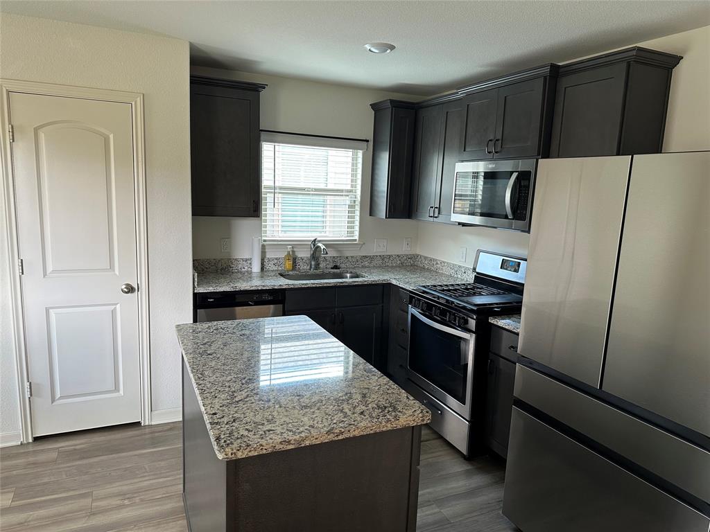 13624 Mineral Road Ponder, TX 76259 - Photo 11 of 26 Kitchen with stainless steel appliances, a sink, light stone counters, a center island, and light wood-type flooring