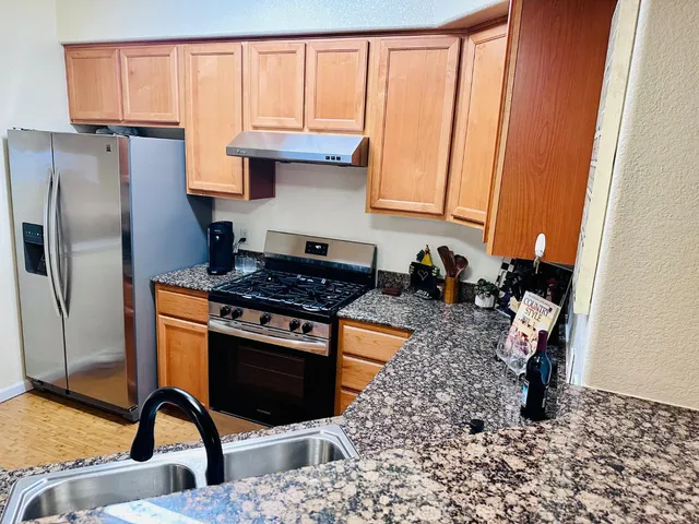 a kitchen with stainless steel appliances granite countertop a stove a sink dishwasher and refrigerator with wooden floor