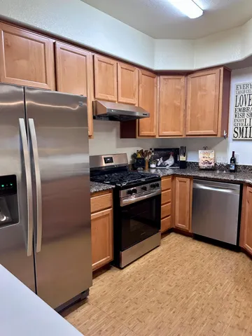 a kitchen with stainless steel appliances granite countertop a stove a sink dishwasher a refrigerator and cabinets with wooden floor