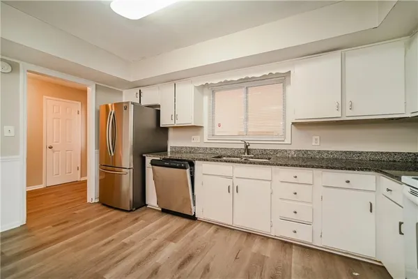 a kitchen with granite countertop a refrigerator sink and white cabinets