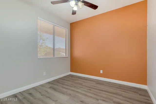 an empty room with wooden floor chandelier fan and windows