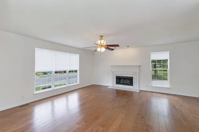 an empty room with wooden floor fireplace cabinet and windows