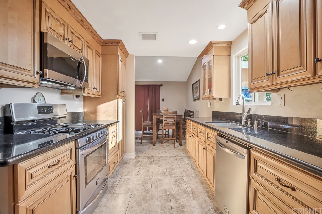 20610 Gresham Street Winnetka, CA 91306 - Photo 11 of 33 a large kitchen with stainless steel appliances granite countertop a stove top oven a sink dishwasher a dining table and chairs with wooden floor
