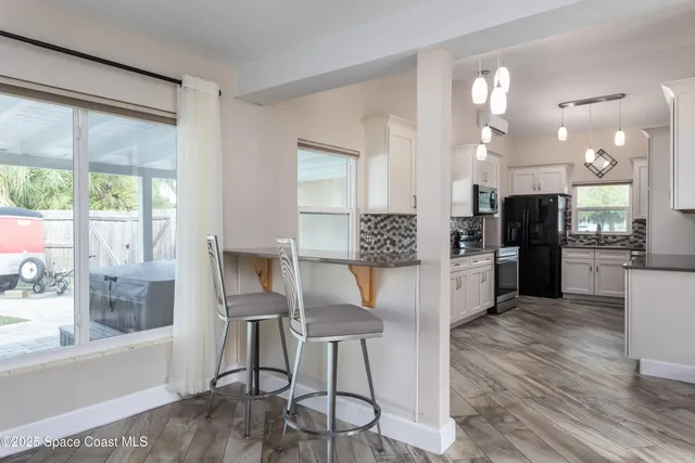 a kitchen with stainless steel appliances kitchen island granite countertop a refrigerator a stove a sink and white cabinets with wooden floor