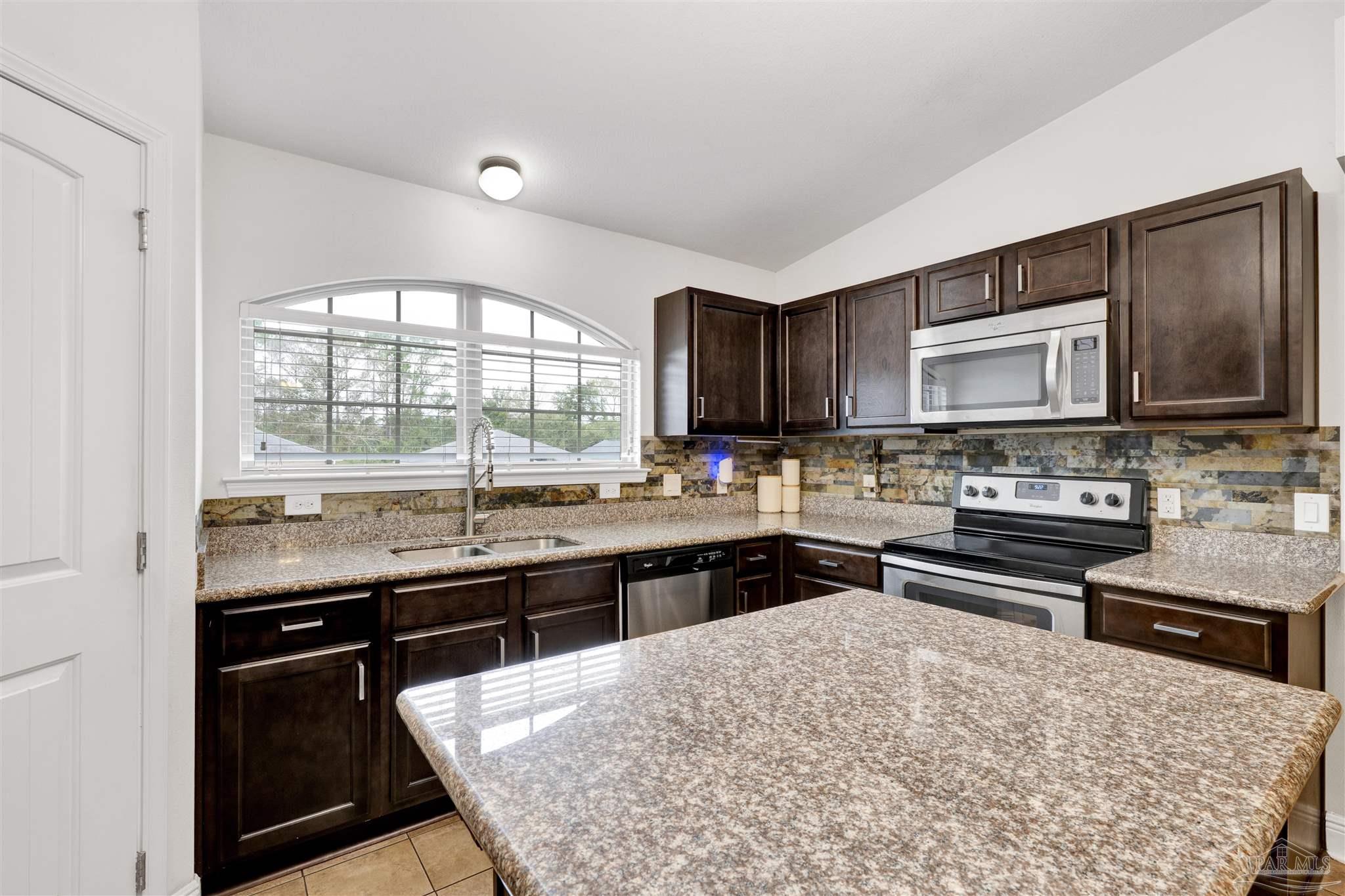 213 Millet Circle Cantonment, FL 32533 - Photo 15 of 33 a kitchen with stainless steel appliances kitchen island granite countertop a stove top oven a sink dishwasher a dining table and chairs with wooden floor
