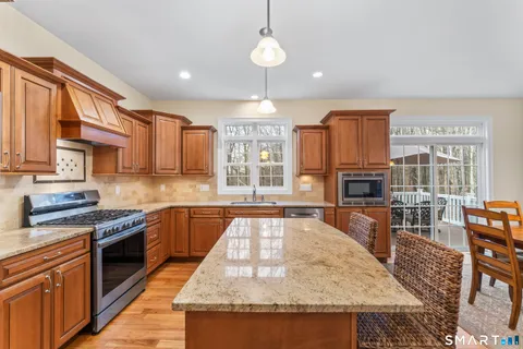 a kitchen with stainless steel appliances granite countertop a stove top oven a sink dishwasher a dining table and chairs with wooden floor