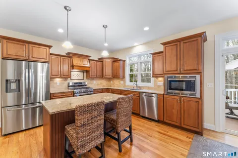a kitchen with stainless steel appliances granite countertop a refrigerator a sink dishwasher a stove and white countertops with wooden floor
