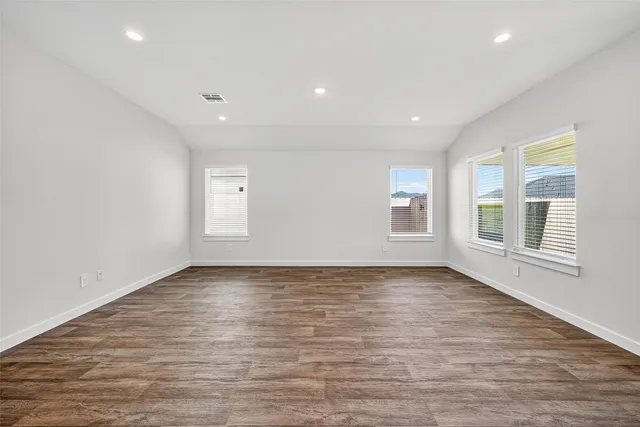 a view of an empty room with wooden floor and windows