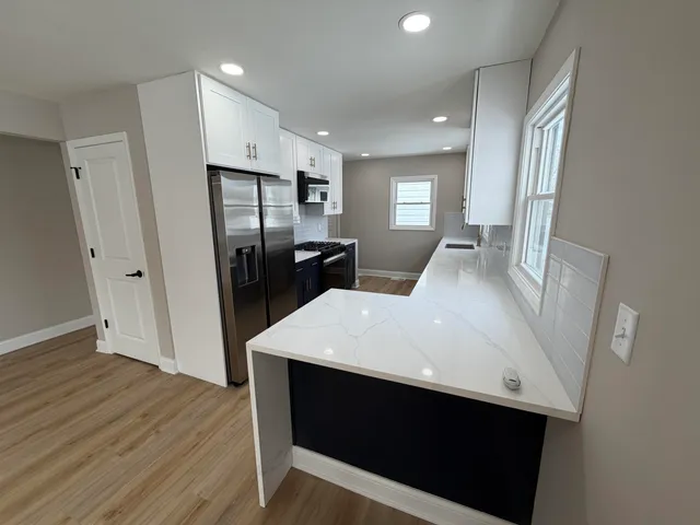 a large white kitchen with a sink a refrigerator and wooden floor