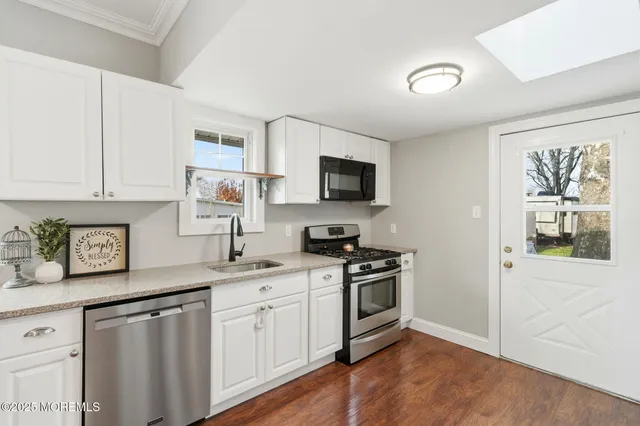 a kitchen with stainless steel appliances granite countertop white cabinets a sink a stove a window and a refrigerator