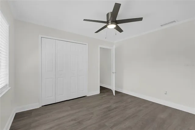 an empty room with wooden floor fan and windows