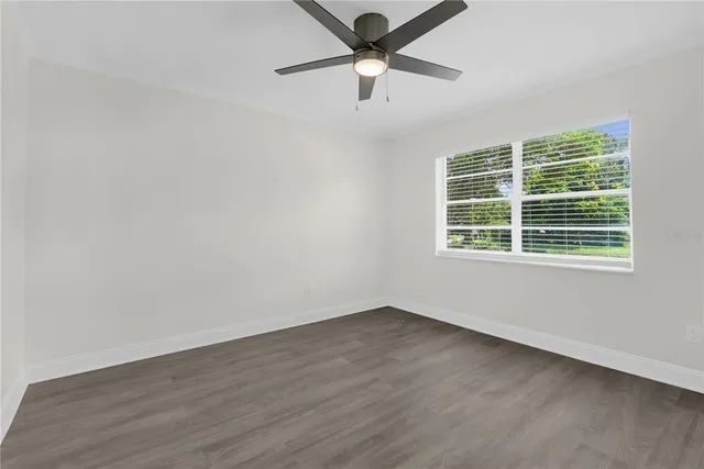 an empty room with wooden floor ceiling fan and windows