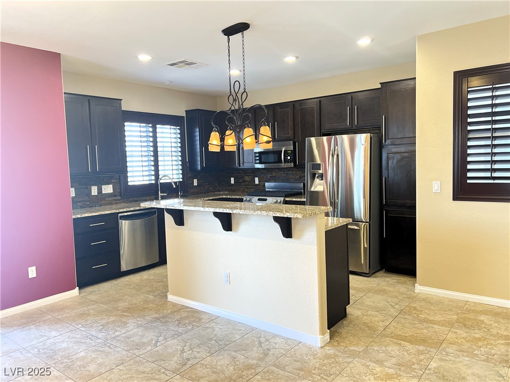 9535 Leaping Lizard Street Las Vegas, NV 89178 - Photo 5 of 37 Kitchen with a chandelier, a kitchen bar, stainless steel appliances, and light stone counters