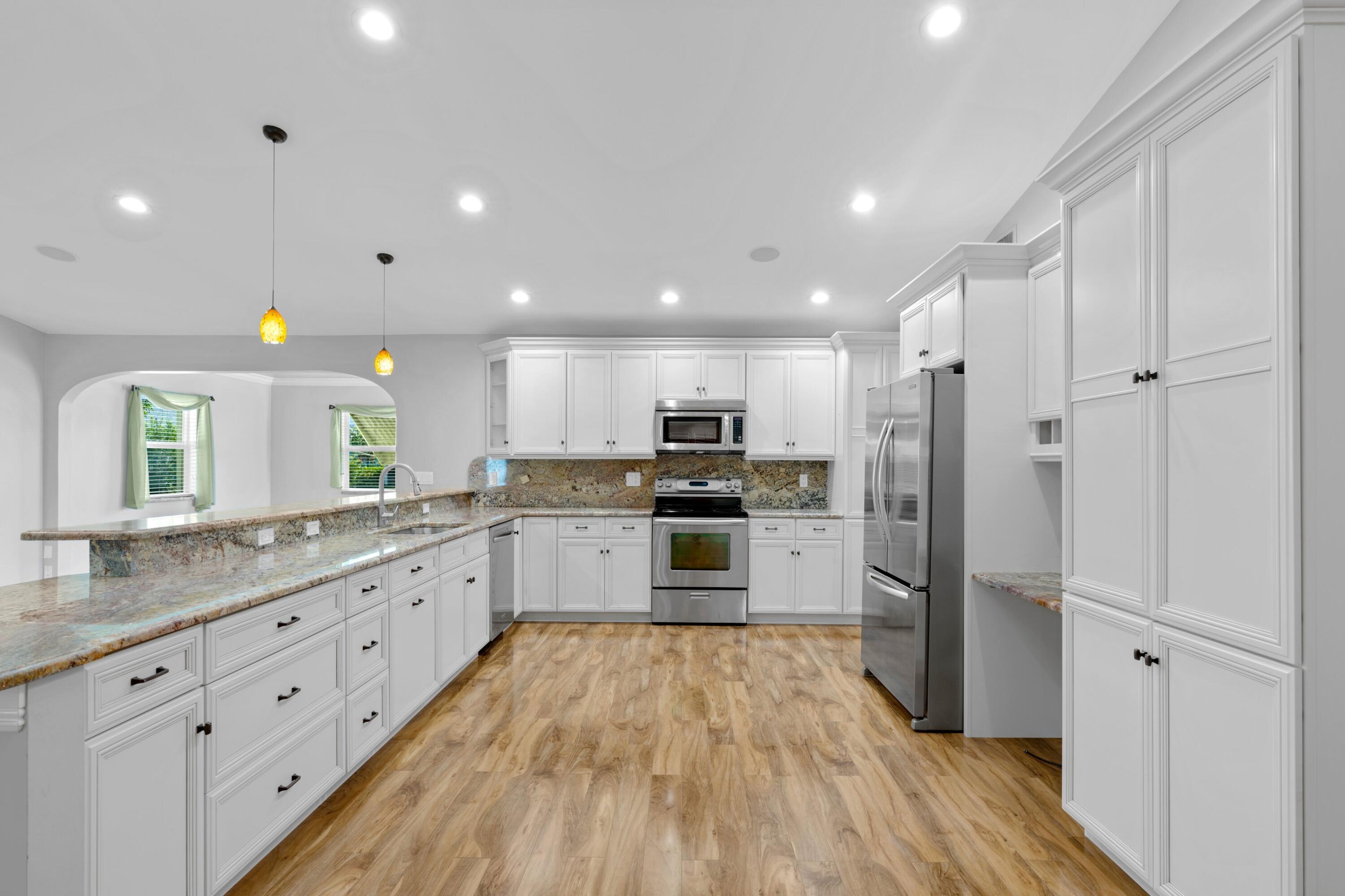 18312 Southeast Eagle Lane Jupiter, FL 33469 - Photo 5 of 17 a kitchen with stainless steel appliances granite countertop a refrigerator a sink dishwasher and white cabinets with wooden floor