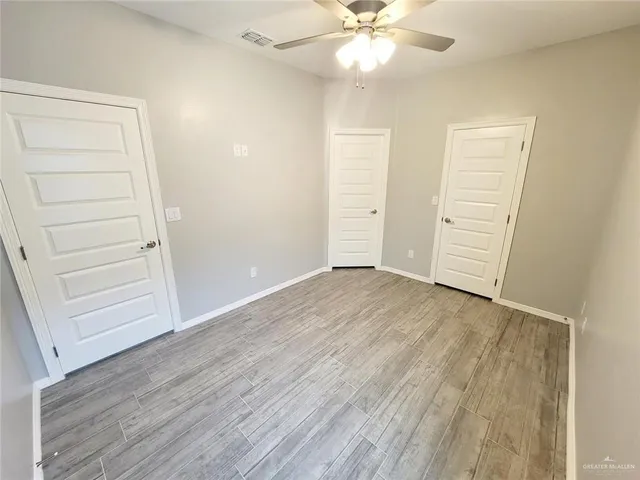 an empty room with wooden floor closet and windows
