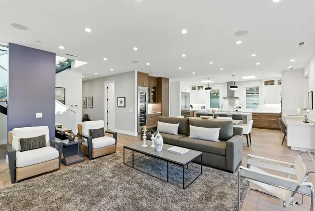 a living room with white couches and kitchen view with wooden floor