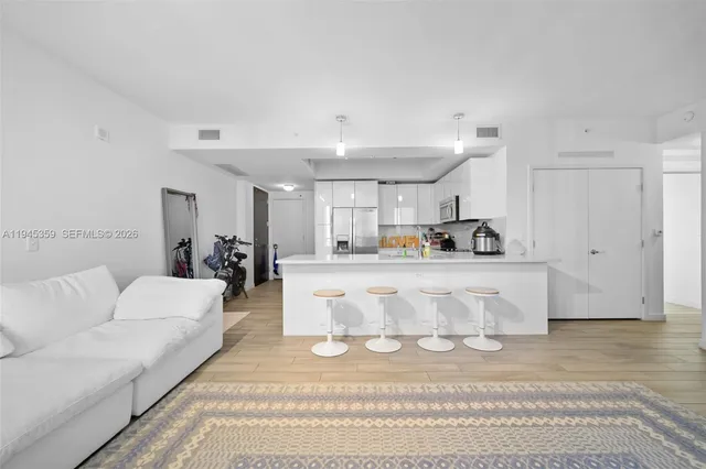 a living room with white couches and kitchen view with wooden floor