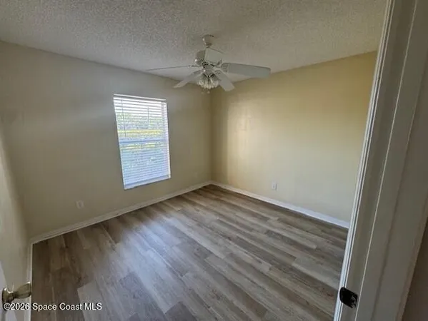 an empty room with wooden floor fan and windows