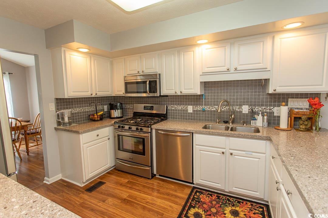 18 Pine Valley Lane Surfside Beach, SC 29575 - Photo 2 of 35 Kitchen featuring appliances with stainless steel finishes, a sink, wood finished floors, white cabinets, and backsplash