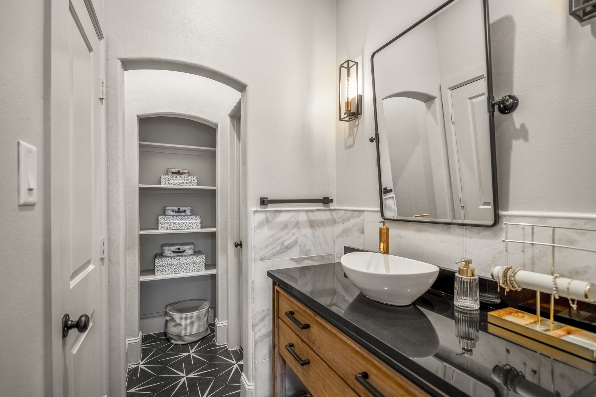3710 Snowden Point Lane Spring, TX 77386 - Photo 26 of 50 This hollywood bathroom features a sleek design with a modern vessel sink on a black countertop and wooden cabinetry. It includes a stylish wall sconce and a large mirror. A spacious walk-in closet with open shelving is visible, providing ample storage. The room is accented with light gray walls and chic tile flooring.