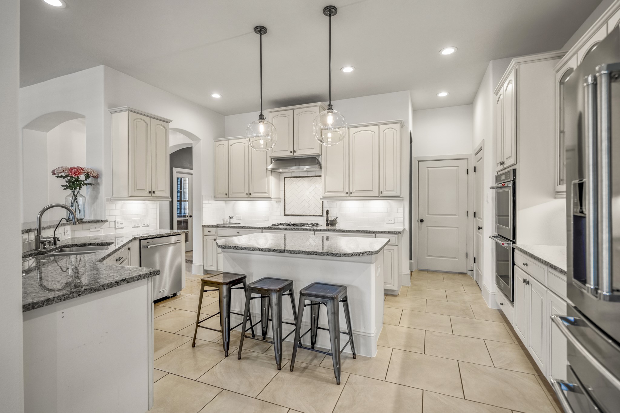 3710 Snowden Point Lane Spring, TX 77386 - Photo 4 of 50 Bright and spacious kitchen featuring modern white cabinetry, granite countertops, and stainless-steel built-in appliances. The central island offers additional seating, and pendant lighting provides a warm ambiance.