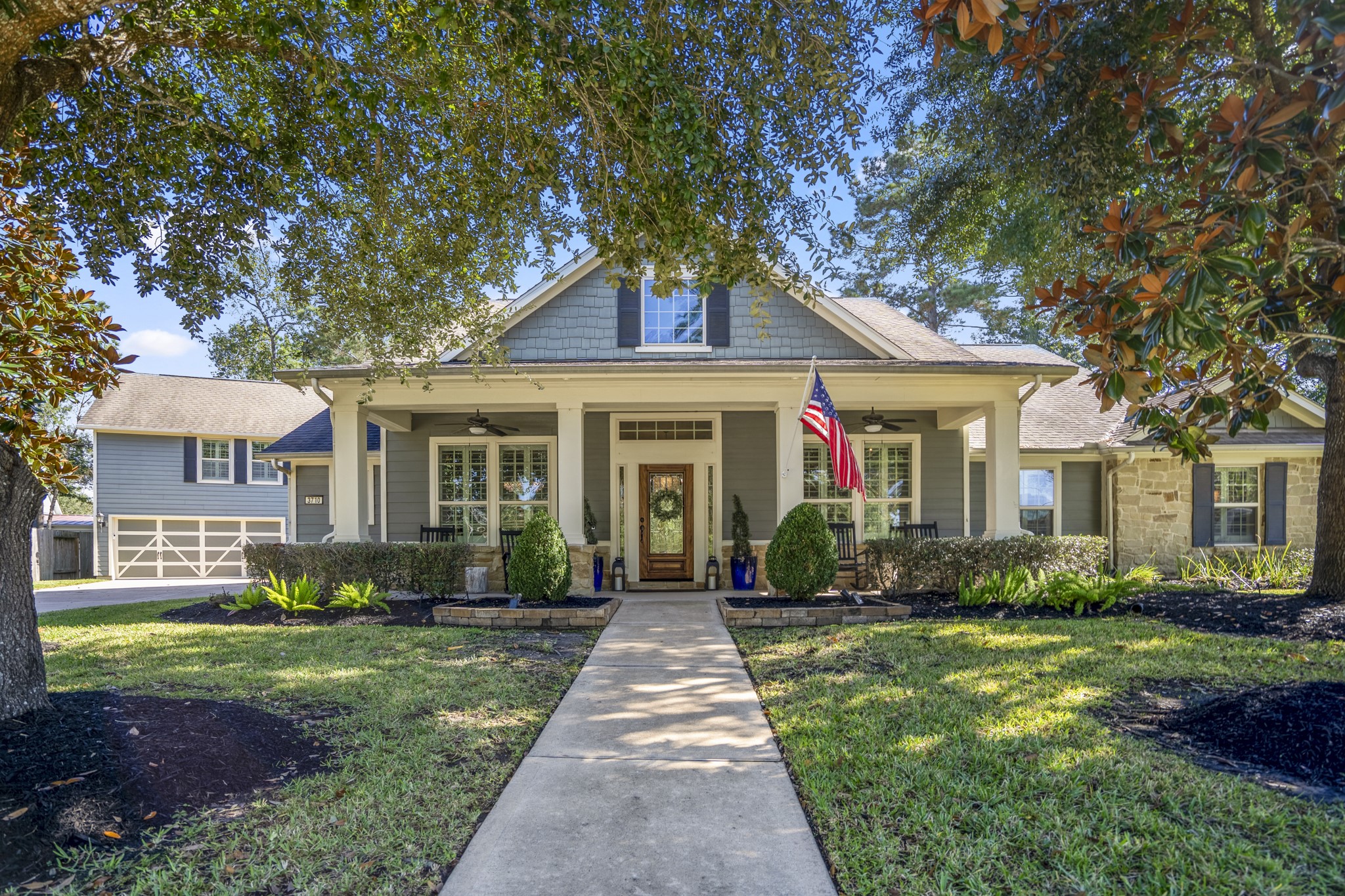 3710 Snowden Point Lane Spring, TX 77386 - Photo 8 of 50 Charming single-story home with a welcoming front porch, set amidst lush landscaping. Features a well-maintained lawn, mature trees, and a classic American flag display.