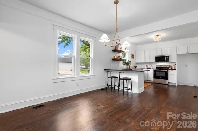 a open kitchen with stainless steel appliances granite countertop a stove top oven a dining table and chairs with wooden floor