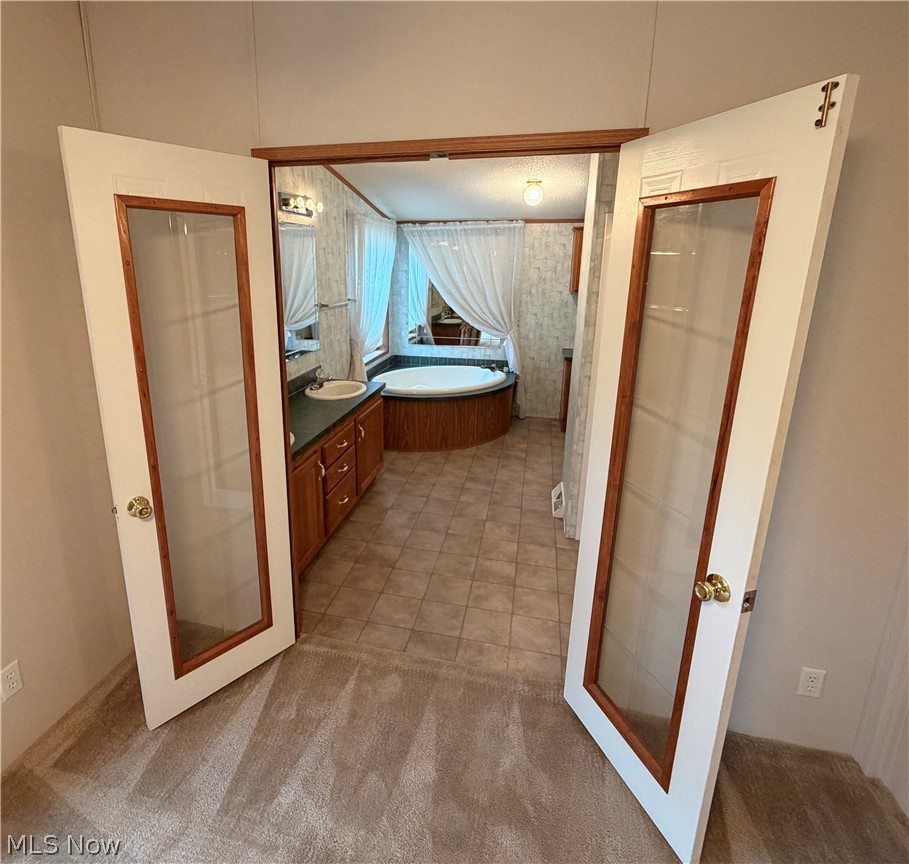 7213 Davis Road Orwell, OH 44076 - Photo 11 of 24 French doors with glass panels open to a bathroom featuring a built-in jetted tub, a vanity with a drop-in sink, and tile flooring