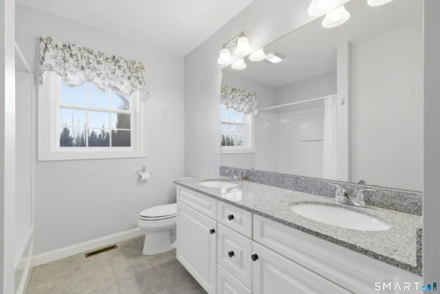a bathroom with a granite countertop double vanity sink mirror and toilet