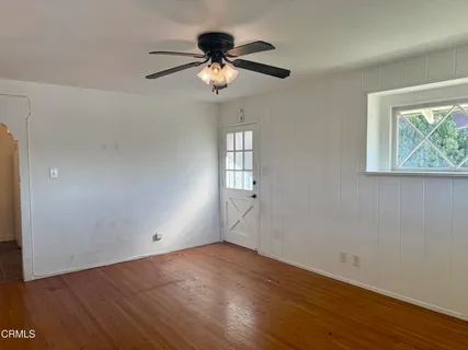 an empty room with wooden floor chandelier fan and windows