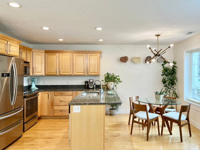 1017 South 275 West Logan, UT 84321 - Photo 6 of 36 Kitchen with a peninsula, stainless steel appliances, dark stone countertops, a kitchen bar, and light wood-style flooring
