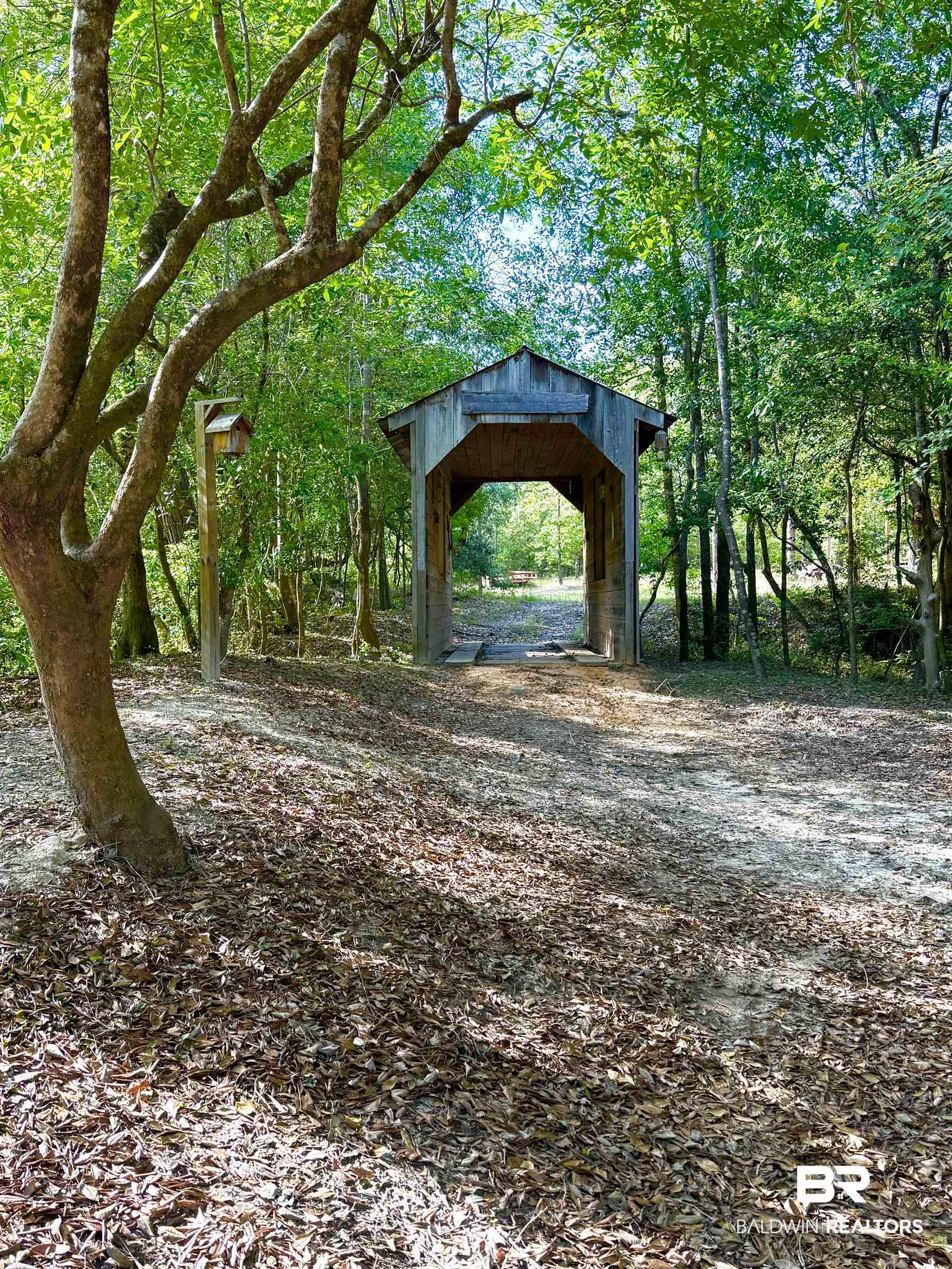 1 Mason Ferry Road Citronelle, AL 36522 - Photo 24 of 40 Wooden covered bridge structure within a wooded landscape, featuring abundant green foliage and a natural ground cover of leaves
