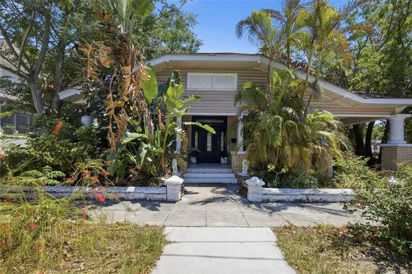 front view of a house with potted plants and a large tree