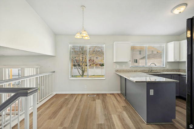 5529 Ridge Hollow Way Kearns, UT 84118 - Photo 3 of 23 Open-concept space featuring wood-finish flooring, a kitchen island with stone countertop, white upper cabinetry, and a white spindle railing