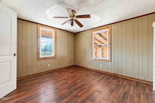 an empty room with wooden floor fan and windows