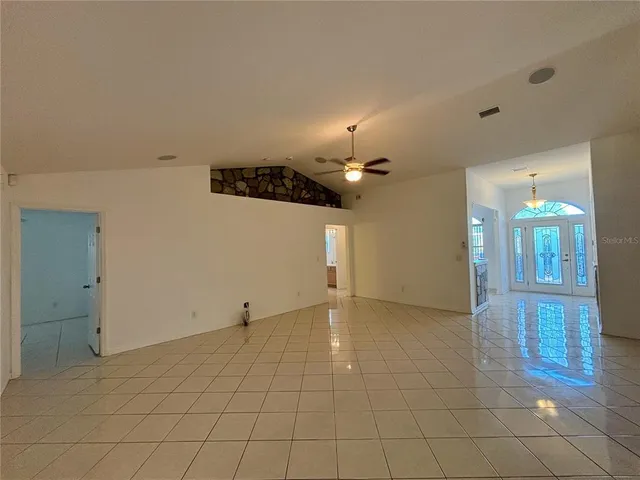 an empty room with kitchen and chandelier fan