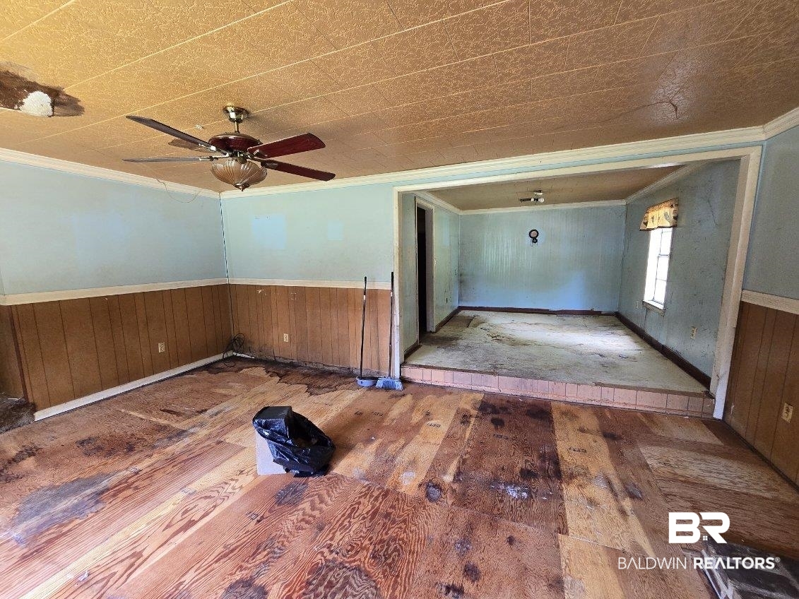 4072 Appleton Road Brewton, AL 36426 - Photo 2 of 7 Empty room featuring hardwood / wood-style floors, crown molding, a wainscoted wall, wooden walls, and ceiling fan