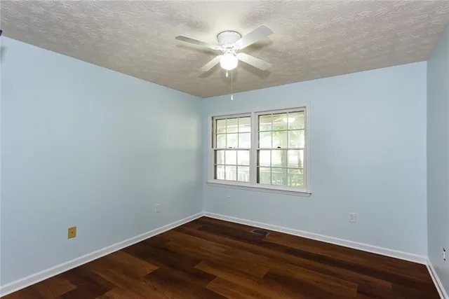 an empty room with wooden floor fan and windows